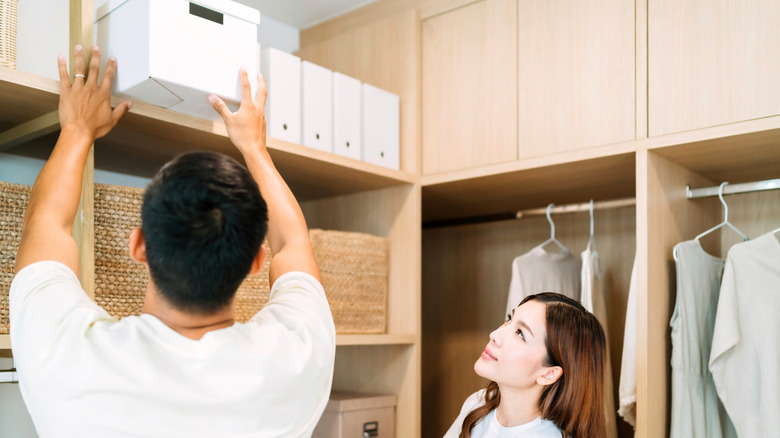 Man placing a box up on the top shelf in a walk-in closet