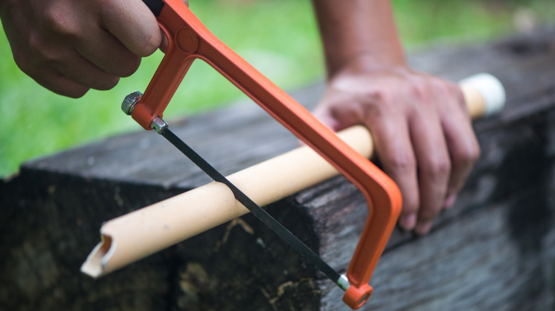 A person cutting a PVC pipe with a saw