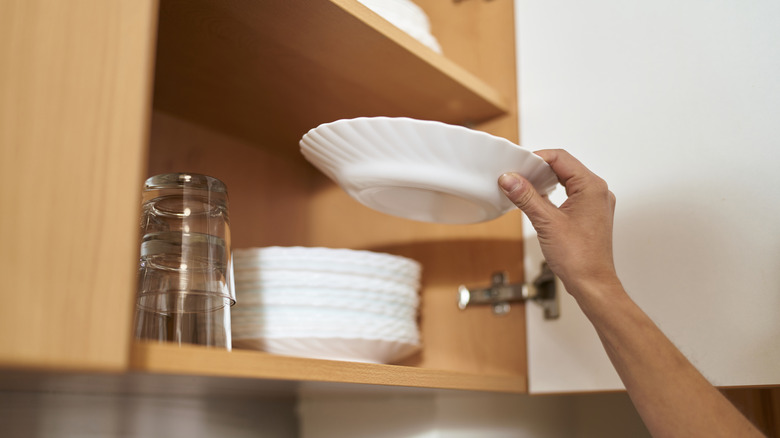 View of person's hand grabbing a bowl from a kitchen cabinet