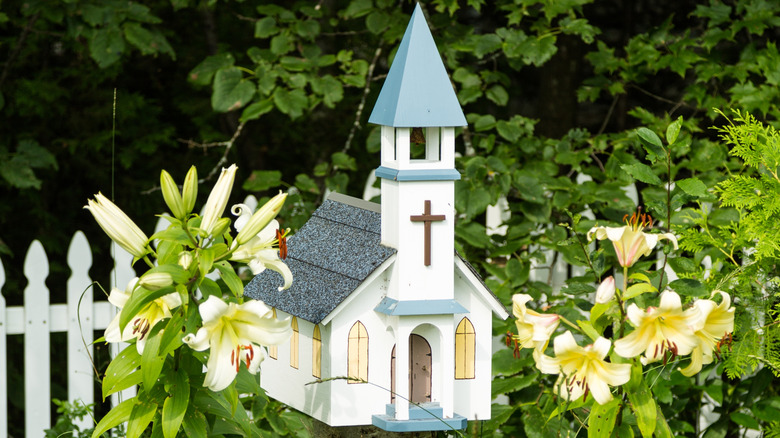 Creative church-inspired birdhouse on a white picket fence with greenery