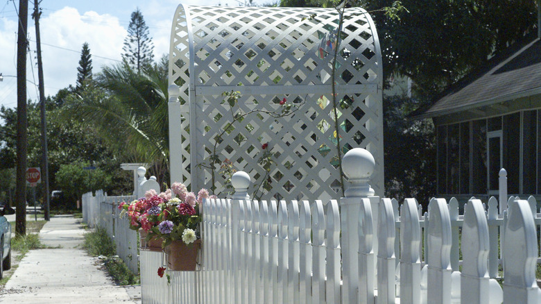 Sidewalk view of home with a white trellis entrance on the white picket fence