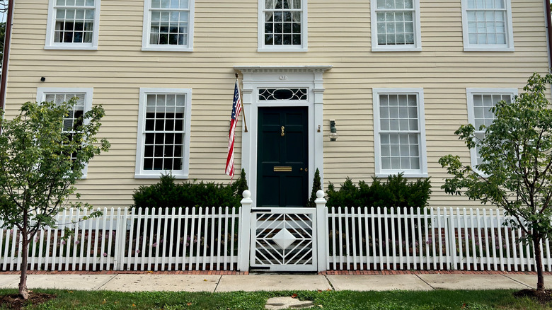 Large house surrounded by white picket fence with a unique gate design