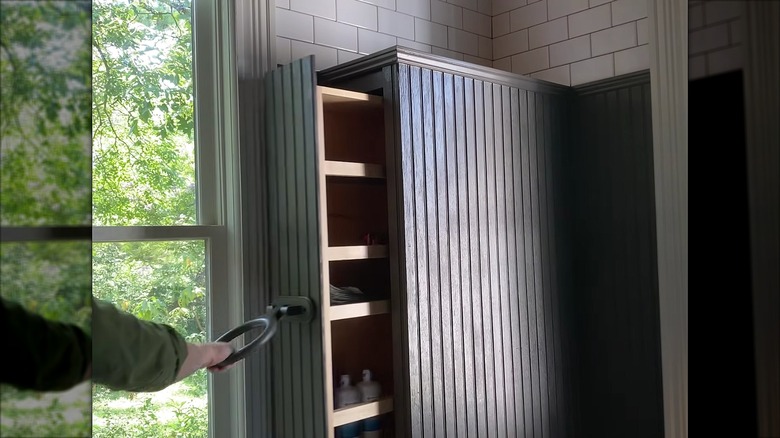 Person pulling hidden shelf from wall in bathroom