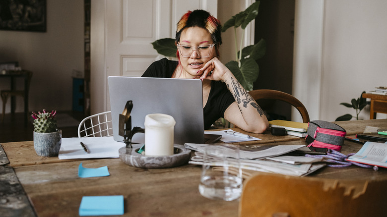 A woman is working at a cluttered home office desk