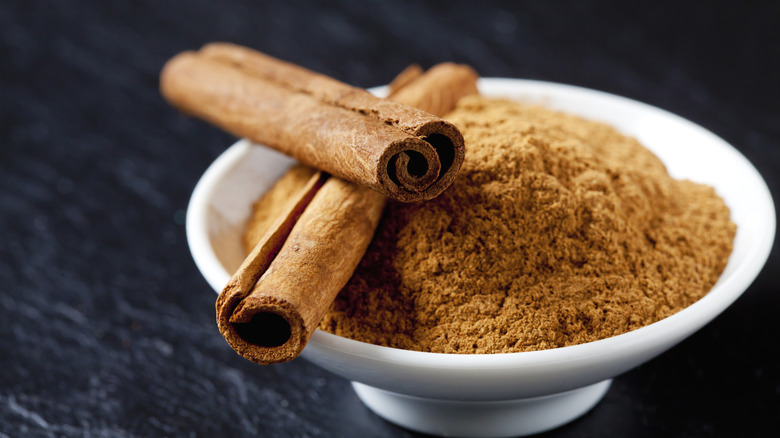 Cinnamon sticks over a bowl of powdered cinnamon