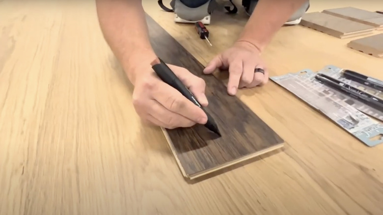 Coloring in scratches on a floor board with a wood stain pen