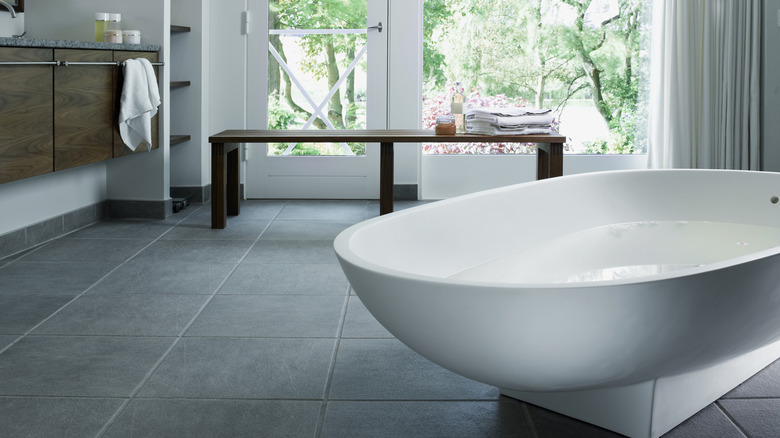 A bathroom with a gray tiled floor and white tubs and walls