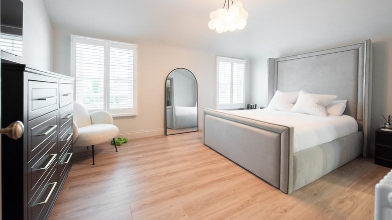 A bedroom with laminate flooring and a large gray bed with white linens