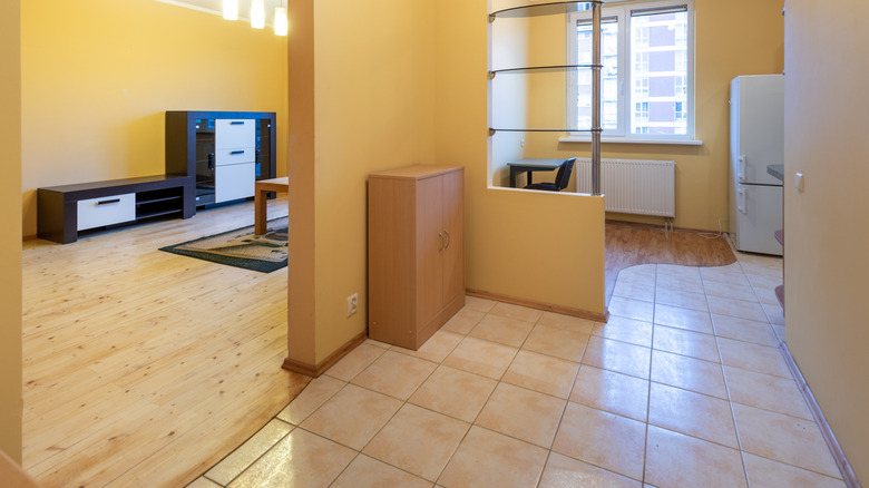 A living room with wood floors and kitchen with tile