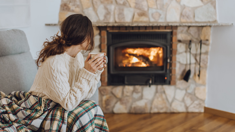 Woman sitting on a couch near her fireplace, holding a coffee mug