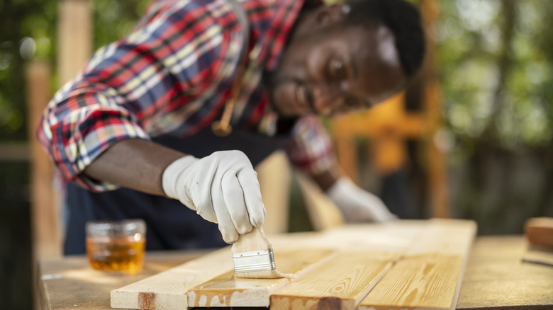 Person applying wood stain with paintbrush