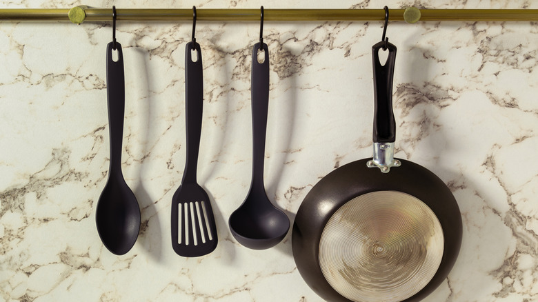 A brass pot rail holding a pan and spatulas against marble backdrop