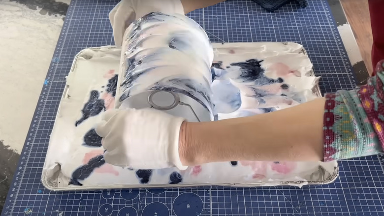 A person rolls a lampshade through a shaving cream dip dye tray