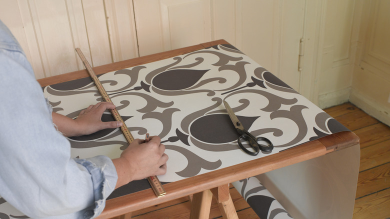 Person cutting and measuring wallpaper