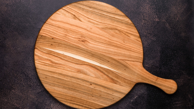 A circular wood charcuterie board with a handle