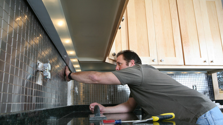 A person installing a kitchen backsplash