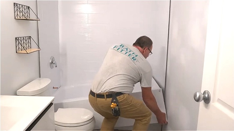 Man installing acrylic bathtub liner insert in white bathroom