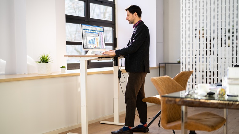 Man working on a height adjustable sit-stand desk in a home office.