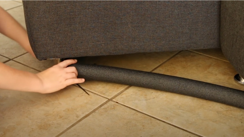 Person tying gray noodle to the leg couch