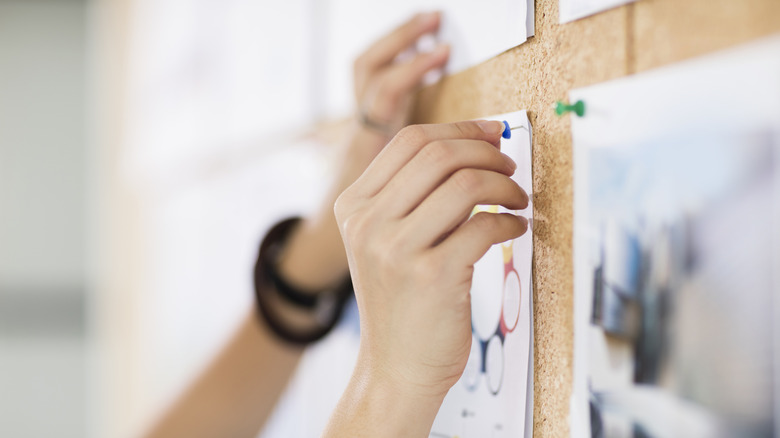 Person pinning paper to cork board