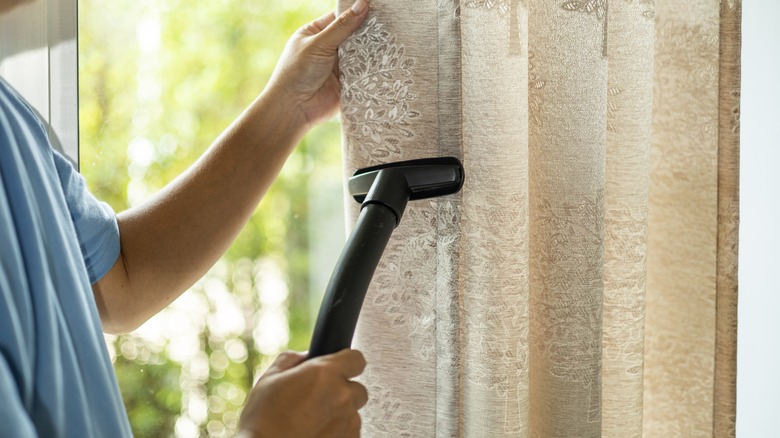 person vacuuming curtains on window