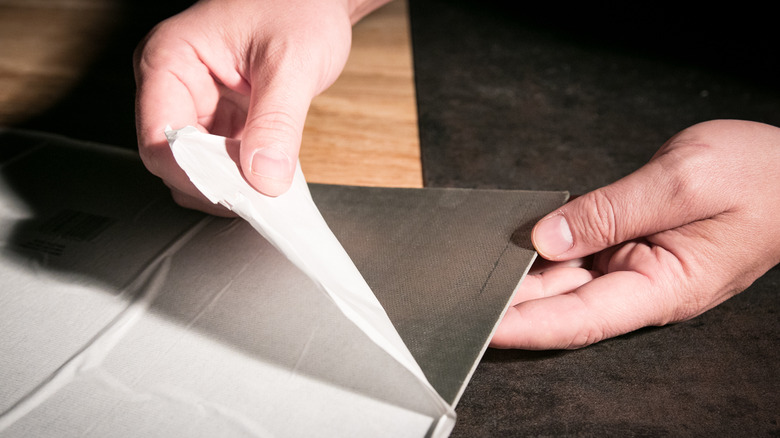 A person is removing the backing from gray peel-and-stick tiles