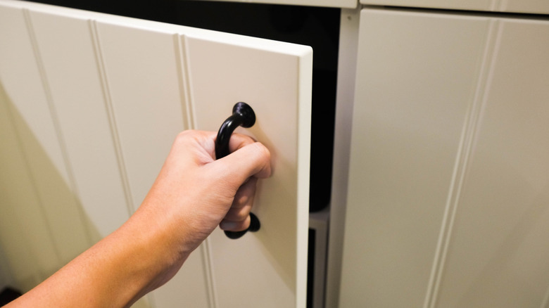 A woman's hand opens plain white cabinets