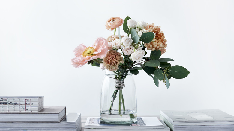 A bouquet sits in a simple glass vase atop books