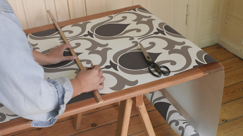 Person preparing wallpaper on table