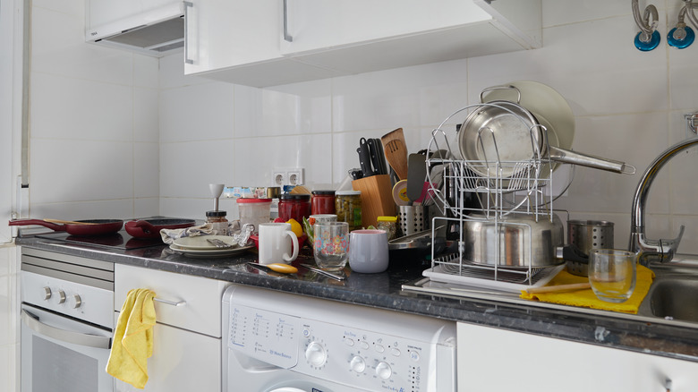 A small kitchen countertop is cluttered with utensils, mugs, and jars