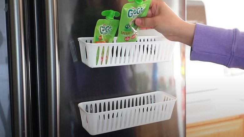 White plastic storage baskets on fridge, hand putting snacks inside