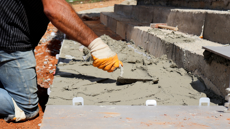 Gloved man using concrete trowel to spread cement on stairs.