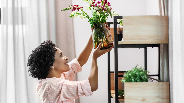 woman adding flowers to shelving unit