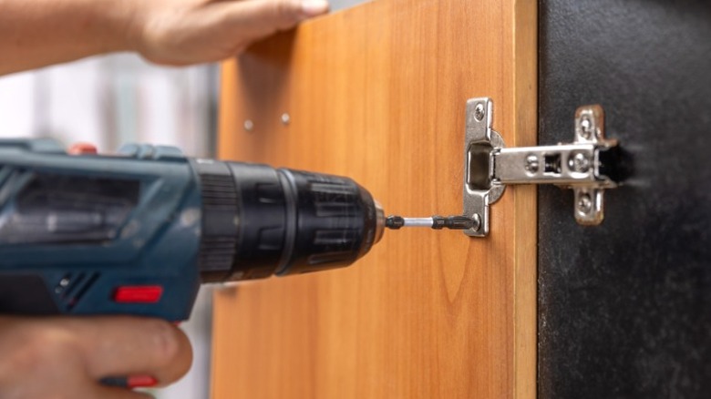 person drilling hinge into wood door