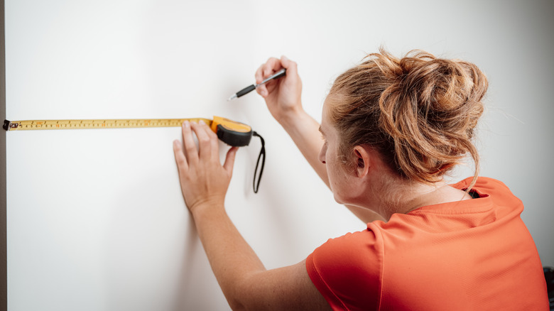 woman using tape measure on blank wall