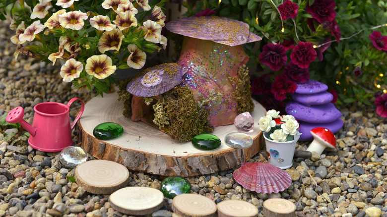 A miniature fairy garden featuring decorative mushrooms, tree slices and pebbles