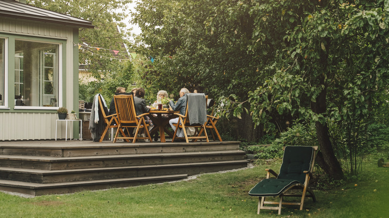 People sitting around a patio table on a deck near a shade tree