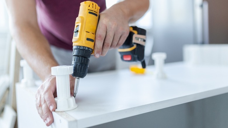 Man attaching white plastic legs to bottom of white cabinet