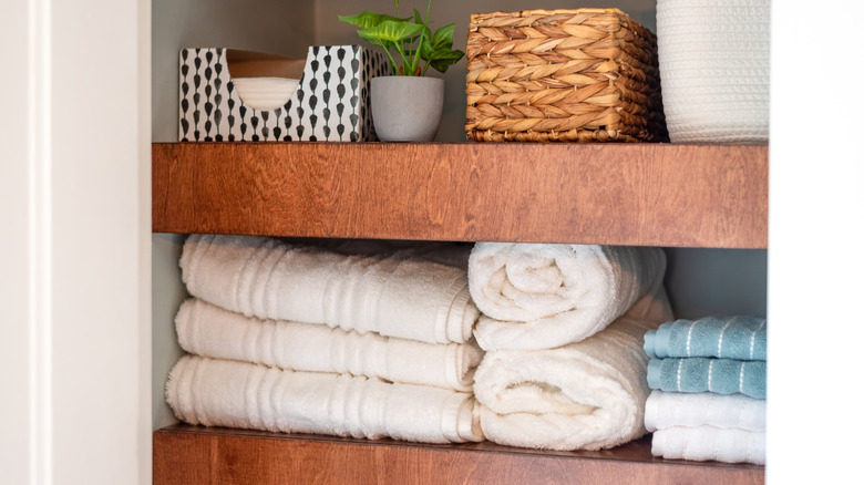 Wooden floating shelves with folded towels, a plant and baskets