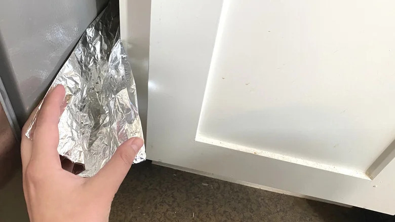 hand cleaning cabinet gap with foil