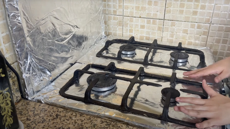 woman laying foil over gas stovetop