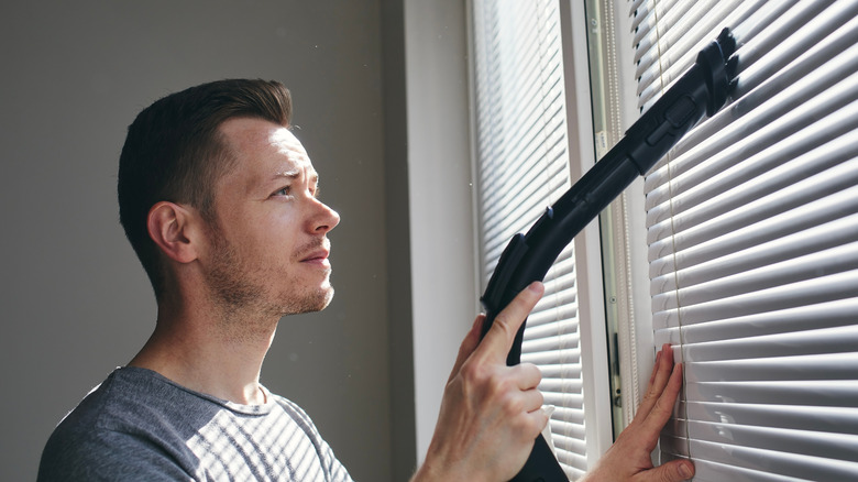 man cleaning blinds vacuum attachment 