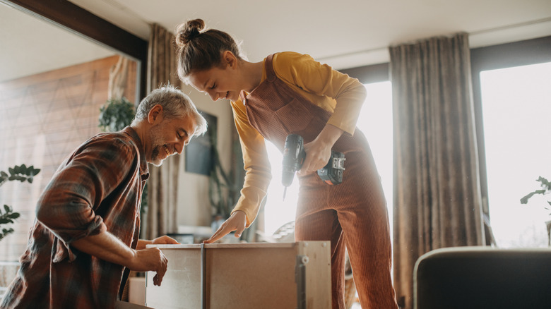 Two people assemble furniture with a drill