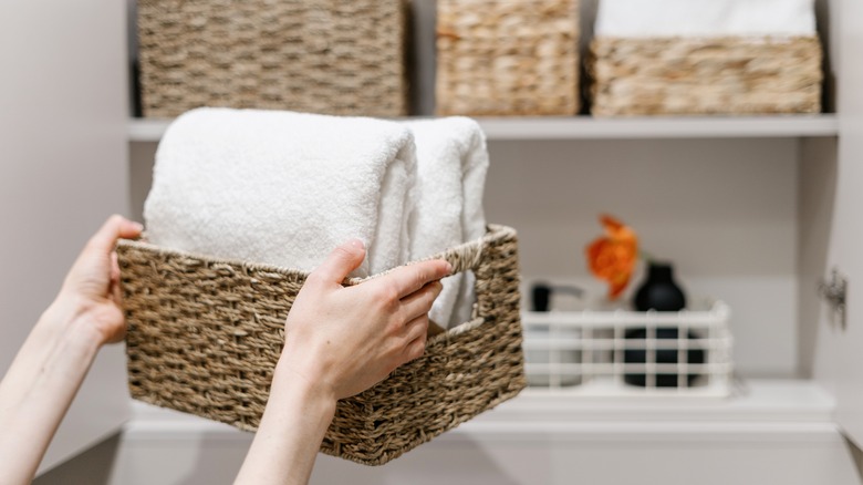 Person storing white towels in wicker basket in closet