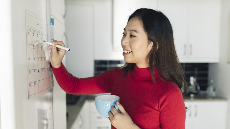 Woman writing on kitchen wall calendar with expo marker