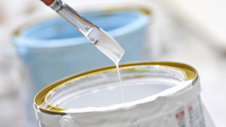 Paint brush dipping into jar of white paint