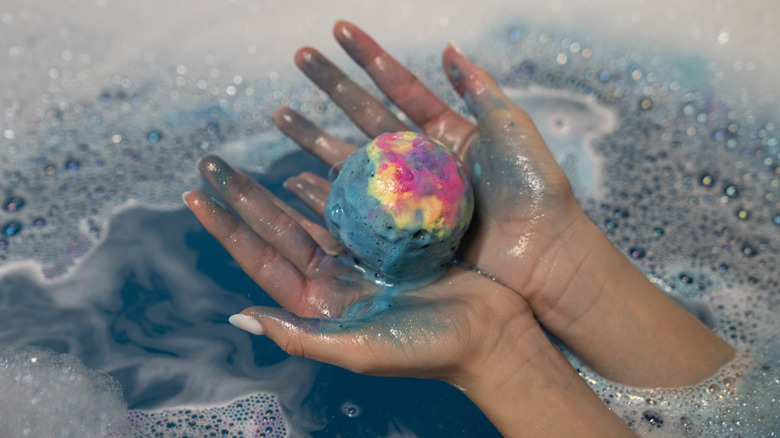 Hands holding a half-dissolved bath bomb in the tub