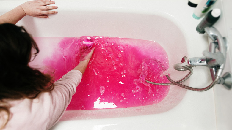 Someone mixing around a pink bathbomb in their bath