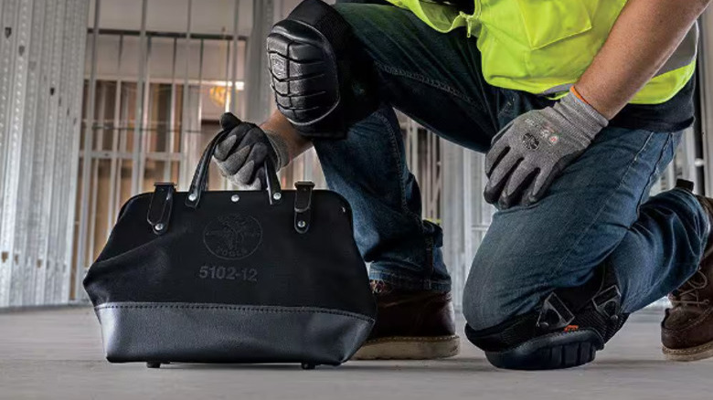 Construction worker picking up a canvas tool bag from the ground