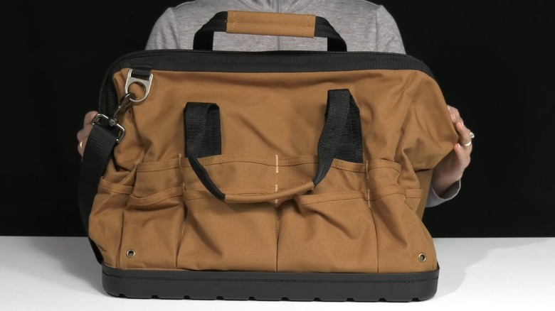 A person holding a molded bottom Carhartt tool bag on a white table with a black background